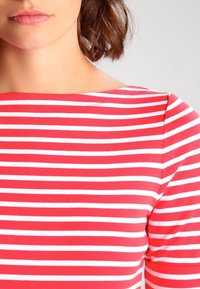 Červenobíle pruhovaný top s širokým výstřihem a přiléhavými rukávy, vyrobený z měkkého, elastického materiálu. Design obsahuje vodorovné pruhy.