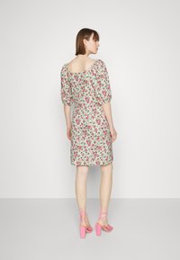 Vestido floral com mangas bufantes, apresentando uma base branca e padrões de flores rosas. O modelo combina-o com sandálias rosa de tiras.