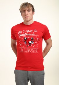 Červené bavlněné tričko s potiskem usměvavé kraví tváře, sněhovými vločkami a textem "Všechno, co chci k Vánocům, je SMÍCH" ve svátečním písmu.