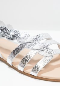 Hopeaken punainen sandaali, jossa on metallinhohtoiset punokset, avoin varvasmuotoilu ja kevyt pehmustettu pohja, jossa on litteä pohja.