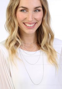 Silberne mehrlagige Kettenhalskette mit unterschiedlichen Längen und Texturen, getragen über einem weißen Hemd von einem Modell.