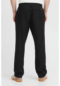 Black, relaxed-fit pants with an elastic waistband. Made of soft fabric, featuring a slight stretch. Accented with a small logo on the back.