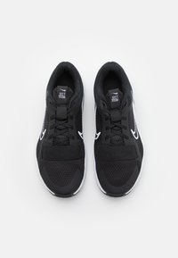 Para czarnych butów biegowych Nike z białymi logo swoosh, siateczkową cholewką, sznurówkami i znaczkami "Just Do It" na językach, pokazane z góry.