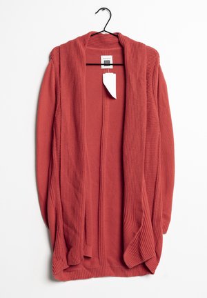 Otwarty sweter z długim rękawem, dziany, w kolorze rdzawej czerwieni, wiszący na czarnym wieszaku z przymocowaną białą metką z ceną.