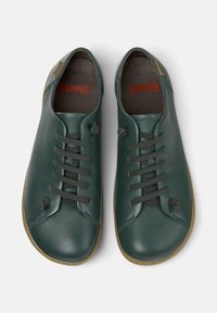 Zapatos de cuero verdes con punta redonda, que cuentan con seis cordones oscuros, una suela de goma marrón y un logo "CAMPER" rojo en el interior.