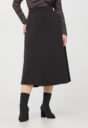 Gonna midi nera a forma A con una texture liscia, abbinata a stivaletti neri alla caviglia. La vita è aderente, scendendo delicatamente all'orlo.