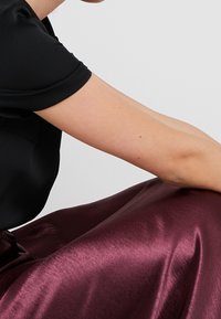 Černý saténový top s krátkými rukávy, doplněný burgundskou lesklou saténovou sukní. Sukně má hladkou texturu a elegantně se vznáší.