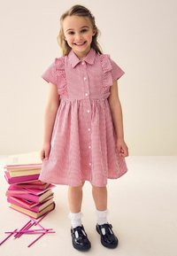 Rotes und weißes Vichy-Karo-Kleid mit Rüschensleeves, durchgehender Knopfleiste und gerafftem Taillenbereich. Schwarze Lackschuhe, weiße Knöchelsocken mit Spitzendekor.