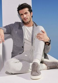 Grau strukturierte Blazer über einem weißen Hemd, kombiniert mit grauen Jogginghosen und grauen Sneakers. Glatte Materialien mit dezenten Mustern und Akzenten.