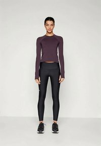 Long-sleeve purple athletic top paired with black form-fitting leggings and black sneakers, featuring a smooth texture and minimalistic design.