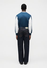 Μπλε σκούρο πουκάμισο μακρυμάνικο με υφασμάτινη υφή και λευκά μανίκια από δίχτυ, σε συνδυασμό με σκούρο μπλε παντελόνι φαρδιάς γραμμής με πλαϊνές τσέπες και λογότυπο στη μέση.