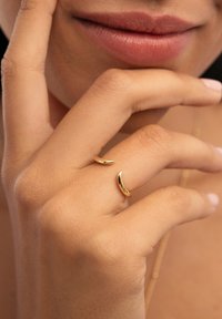 Anillo de oro con forma de media luna minimalista, acabado pulido, llevado en el dedo; tono de piel visible, enfoque suave en la mano.