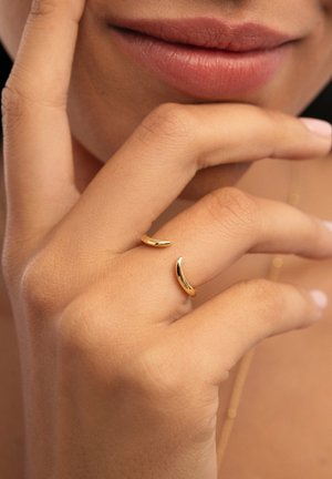 Anillo de oro con forma de media luna minimalista, acabado pulido, llevado en el dedo; tono de piel visible, enfoque suave en la mano.