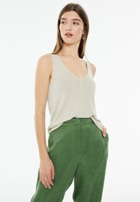 Beige v-kaula tankki, jossa on kiiltävä pinta, yhdistettynä korkeavyötäröisiin vihreisiin housuihin, joissa on pehmeä, sileä kangas.