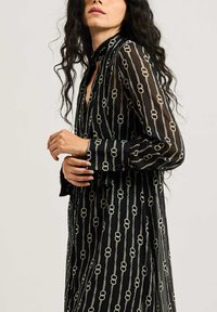 Abito camicia nero trasparente con maniche lunghe, caratterizzato da un motivo a catena argentato. Finitura con colletto e polsini bottonati.