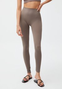 Geribbelde, bruine leggings met een hoge tailleband, aansluitend ontwerp en een gladde textuur. Gecombineerd met zwarte platte sandalen met dunne banden.