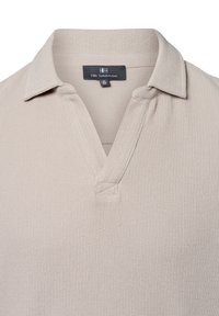 Beige gerippte Polohemd mit einem Kragen und einer halben Knopfleiste. Verfügt über einen strukturierten Stoff und ein Etikett mit der Aufschrift "Nils Sundström."