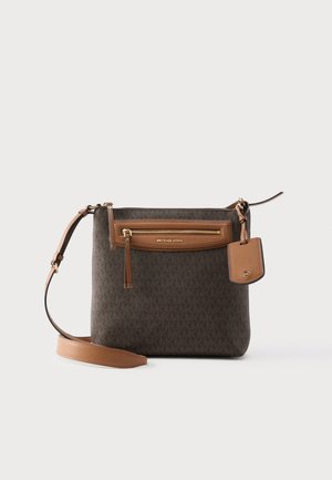 Ruskea Michael Kors -laukku säädettävällä olkahihnalla, etutaskulla ja kiinnitetyllä nahkalisävarustekilvellä, valkoista taustaa vasten.