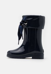 Botte en caoutchouc waterproof bleu marine avec une finition brillante, ornée d'un accent en nœud satiné en haut et d'une semelle texturée pour une meilleure adhérence.