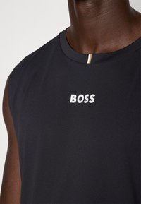 Haut sans manches bleu marine foncé en tissu texturé, comportant un logo "BOSS" blanc sur la poitrine et un accent multicolore au niveau du col.