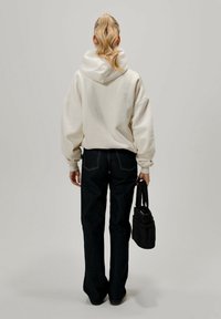 Oversized krämfärgad hoodie med dragsko i huvan, kombinerad med mörkblå jeans med raka ben och en liten svart handväska.