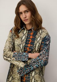Srajca s potiskom mešanice kačjega in leopardjega vzorca v nevtralnih, modrih in oranžnih tonih, z različnimi tkaninami in strukturiranim ovratnikom.