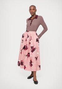 Brown knit polo top with a burgundy collar; pink floral print maxi skirt with black accents; model wearing black flats.