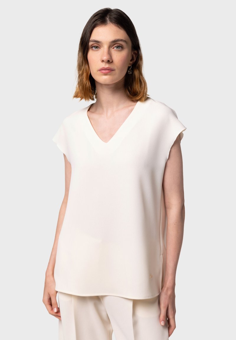 Halenka s výstrihom do V, bez rukávov, vyrobená z mäkkej, štruktúrovanej off-white látky. Má voľný strih a nenápadný detail loga na leme.