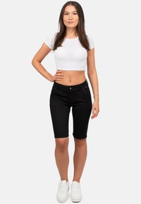Bermuda shorts en denim noir avec une coupe ajustée, fermeture à bouton sur le devant, et deux poches avant, associés à un t-shirt crop blanc et des baskets blanches.