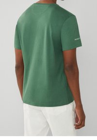 Camiseta de algodón verde con mangas cortas, escote redondo y detalles de costura sutiles. Logo "Hackett" en blanco en la manga izquierda.