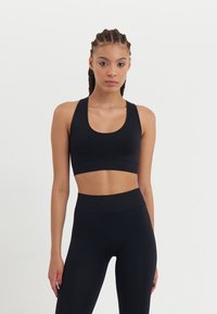 Black sports bra and high-waisted leggings made from stretchy, smooth fabric, featuring a scoop neckline and minimal stitching detail.