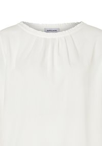 Witte blouse met een ronde halslijn, voorzien van een rimpelrand. Gladde stof met een lichte doorschijnendheid en geplooide details rond de hals.