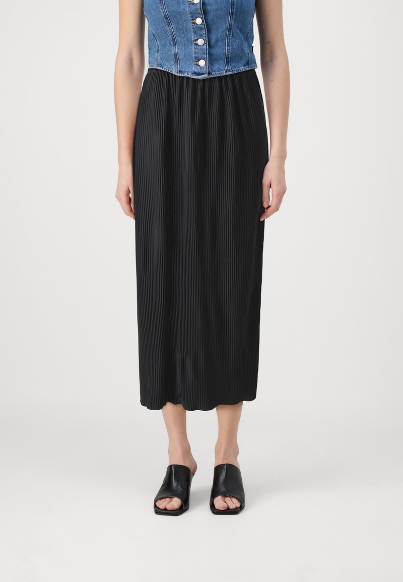 Svart plisseret midi-nederdel med en glat tekstur og ribbet design. Parret med åbentåede sorte slide-sandaler. Denimtop delvist synlig.