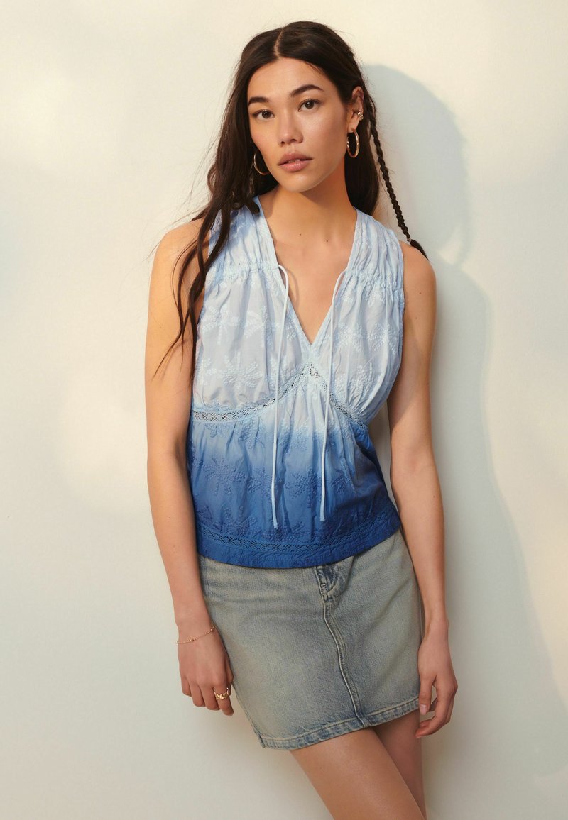 Top senza maniche di colore azzurro chiaro con effetto sfumato a ombre, dettagli in pizzo e scollatura con cordoncino; abbinato a una gonna di jeans.