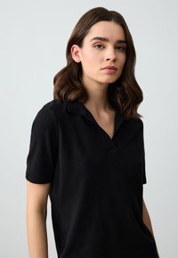 Polo shirt nera realizzata in tessuto morbido, con colletto e maniche corte, dalla vestibilità rilassata e una texture sottile.