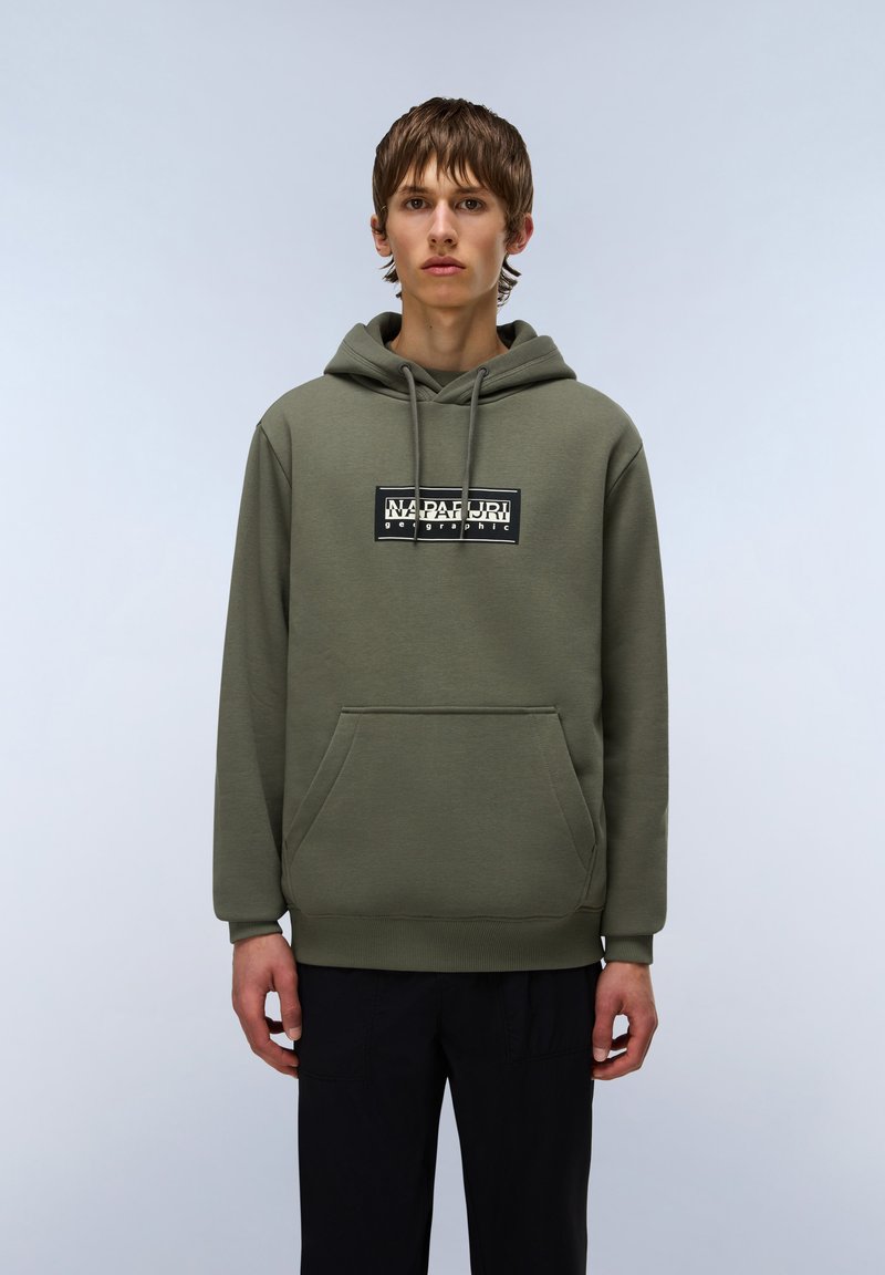 Hoodie vert en tissu doux, présentant une poche kangourou à l'avant et une étiquette noire imprimée avec un texte blanc sur la poitrine.