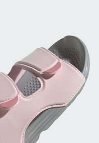 Sandali rosa chiaro con cinturini in velcro, dotati di una suola grigia testurizzata e perforazioni per la traspirabilità. Materiale liscio e morbido.