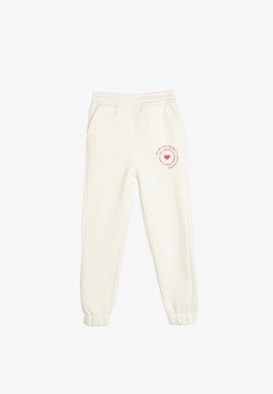Pantalones de chándal de color crema, hechos de una tela suave. Presentan una cinturilla elástica, bolsillos laterales y un diseño impreso con un corazón en la pierna izquierda.