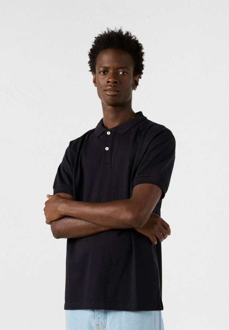Polo shirt nero a maniche corte con colletto, tre bottoni e un piccolo logo. Realizzato in tessuto liscio, con una vestibilità classica.
