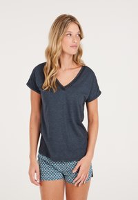 T-shirt a v collo blu scuro con maniche corte arrotolate, realizzata in tessuto morbido. Abbinata a pantaloni corti a fantasia nel design geometrico blu e bianco.