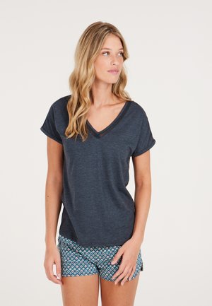 T-shirt a v collo blu scuro con maniche corte arrotolate, realizzata in tessuto morbido. Abbinata a pantaloni corti a fantasia nel design geometrico blu e bianco.