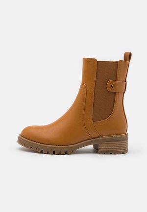Ankelstøvle i tanfarvet læder med elastisk sidepanel, dekorativ rem med knap, trækstrop samt chunky lav hæl i træ og gummisål med kraftigt mønster.
