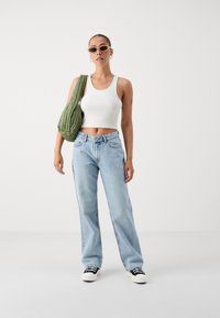 Λαμπερά μπλε φαρδιά τζιν παντελόνια, λευκό ριμπά crop top και πράσινη επενδεδυμένη τσάντα ώμου. Μαύρα και λευκά αθλητικά παπούτσια με λεπτομέρεια κορδονιών.