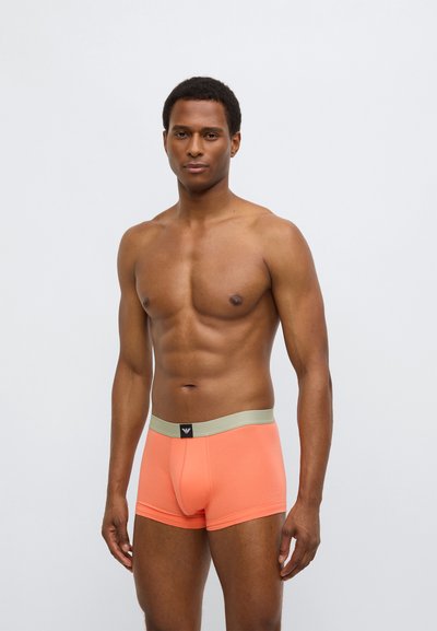 Cuecas boxer de algodão laranja com cintura elástica em verde claro contrastante. O tecido parece suave e ajustado, exibindo um pequeno logótipo na cintura.