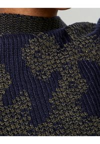 Primo piano di un maglione lavorato a maglia blu e oliva con un motivo a camouflage testurizzato e scollo a coste.