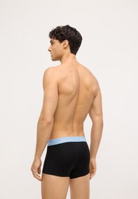 Čierne boxerky so svetlomodrým pásom s logom Calvin Klein, vyrobené z hladkého materiálu a s priliehavým strihom, zobrazené zozadu.