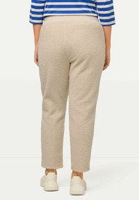 Beige Fleece-Hosen mit strukturierter Oberfläche, schmal zulaufendem Bein und elastischem Bund, kombiniert mit weißen lässigen Sneakers.