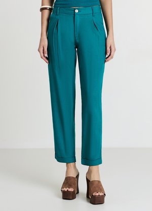 Pantalon plissé bleu sarcelle avec une coupe décontractée, doté de poches avant et d'ourlets avec revers. Associé à des talons compensés marron.