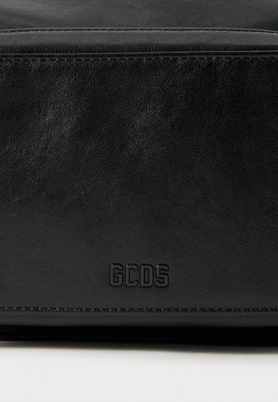 Borsa in pelle nera con una superficie liscia, logo impresso "GCDS" sul davanti e cuciture a contrasto lungo i bordi.