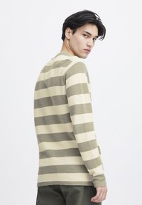 Langermet stripete genser i beige og olivengrønn, laget av teksturert strikket stoff. Har brede horisontale striper og ribbestrikkede mansjetter.
